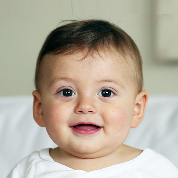 A baby with short hair, grinning widely, conveying joy and innocence, with a soft background.