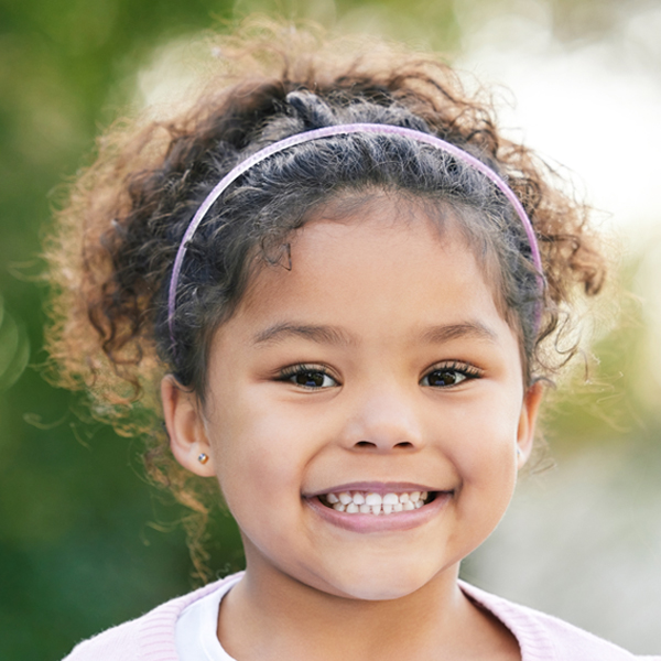 A young girl with curly hair and a headband, beaming with a bright smile, radiating happiness.