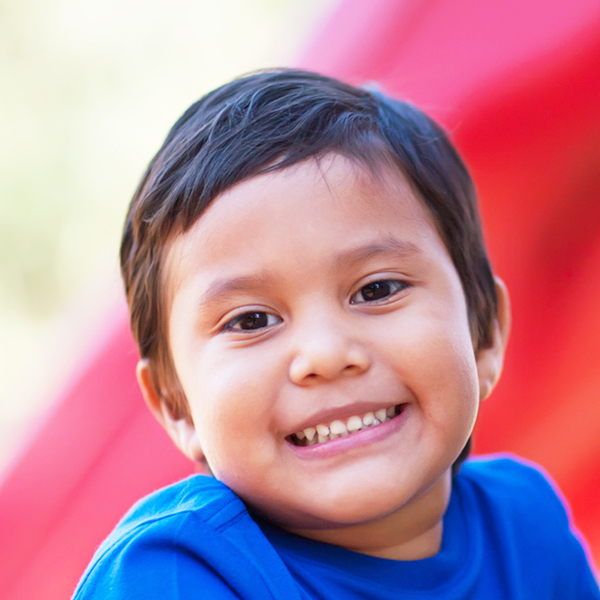 A smiling boy with short hair, looking directly at the camera with a joyful expression, set against a colorful background.