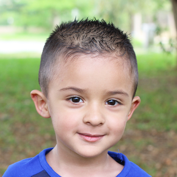 A young boy with short hair, presenting a gentle smile, looking calm and cheerful in a natural setting.