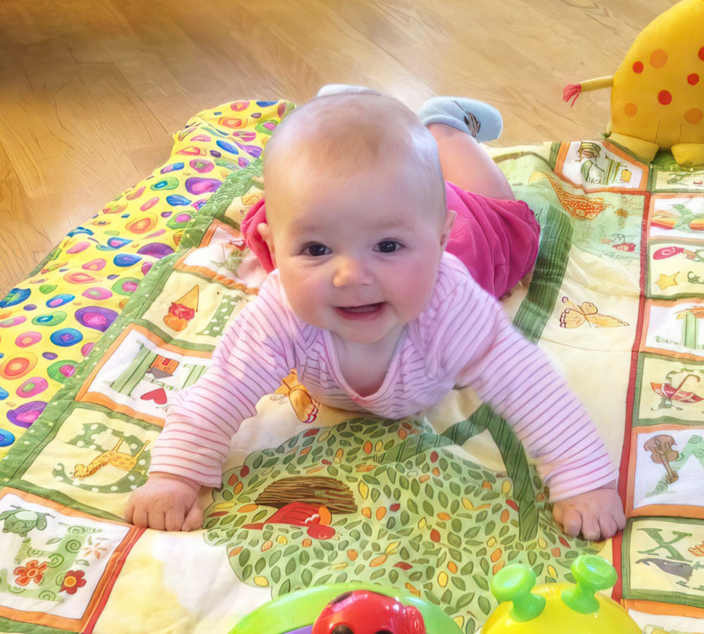 A cheerful baby on a colorful play mat, propped up on her arms and smiling, enjoying playtime.