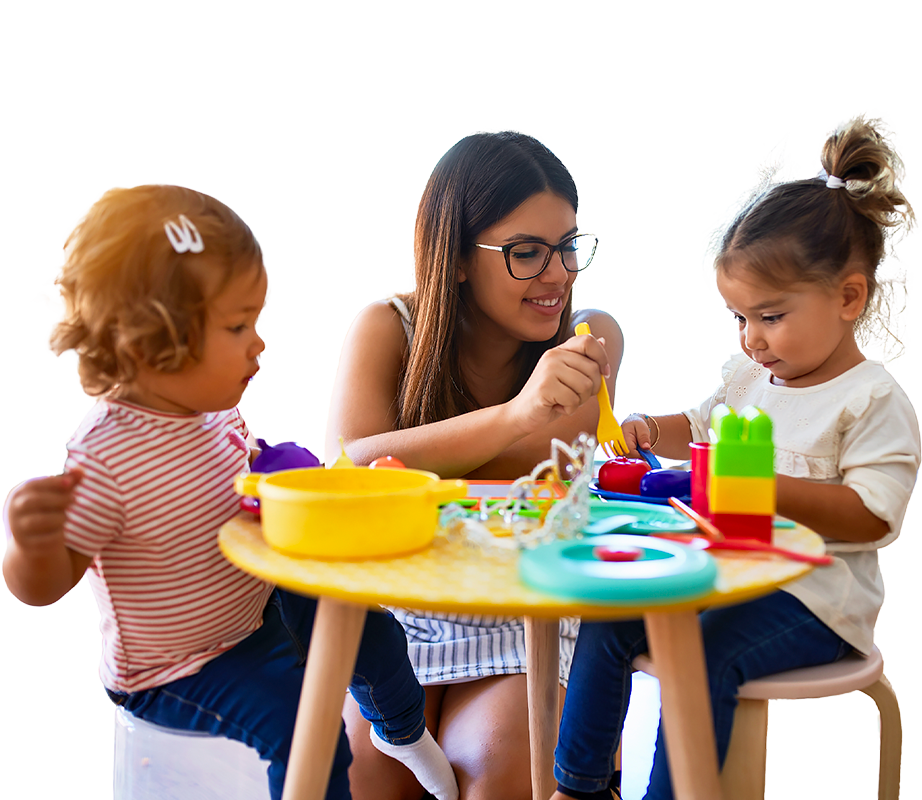 A teacher assists two young girls at a table, surrounded by colorful toys and playful creativity.