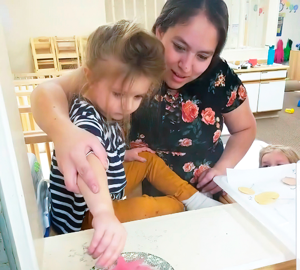 A child and a teacher engage in a fun art activity, collaborating and sharing smiles at a tabletop.