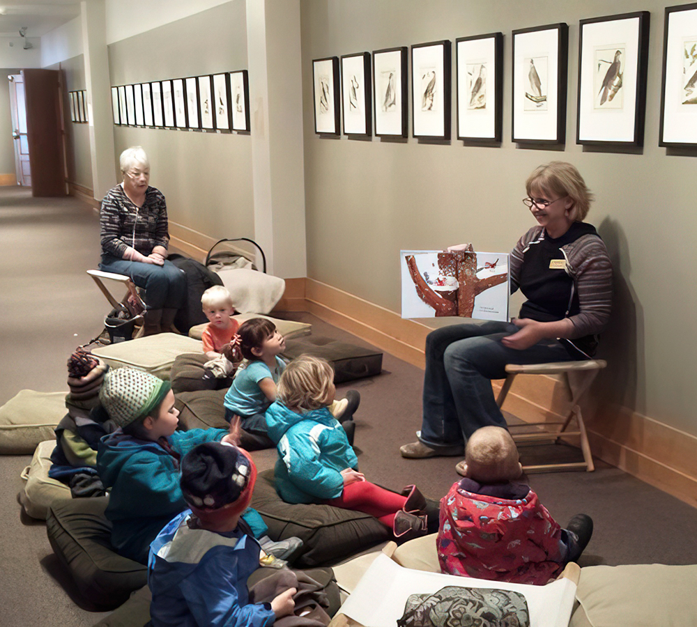 A teacher captivates a group of young children sitting on the floor in a gallery, surrounded by artwork on the walls.