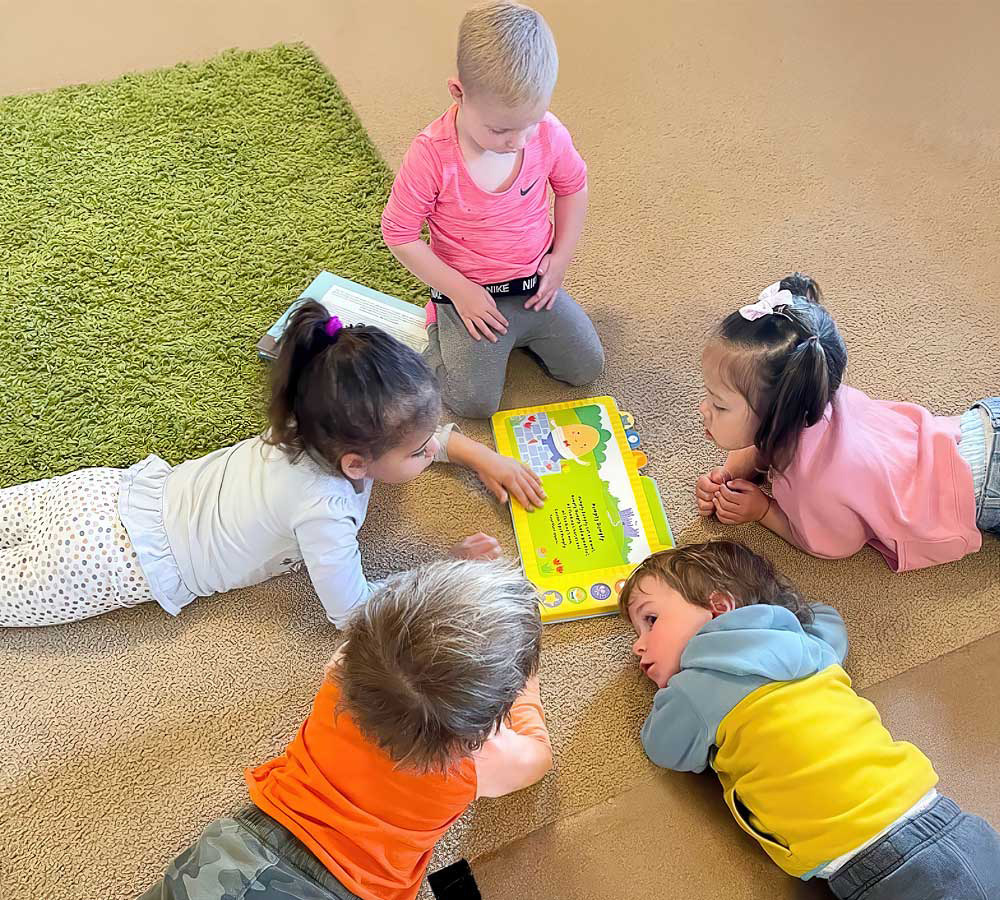 A group of children gathered on the floor, engaged in reading a colorful book together, showing curiosity and collaboration.