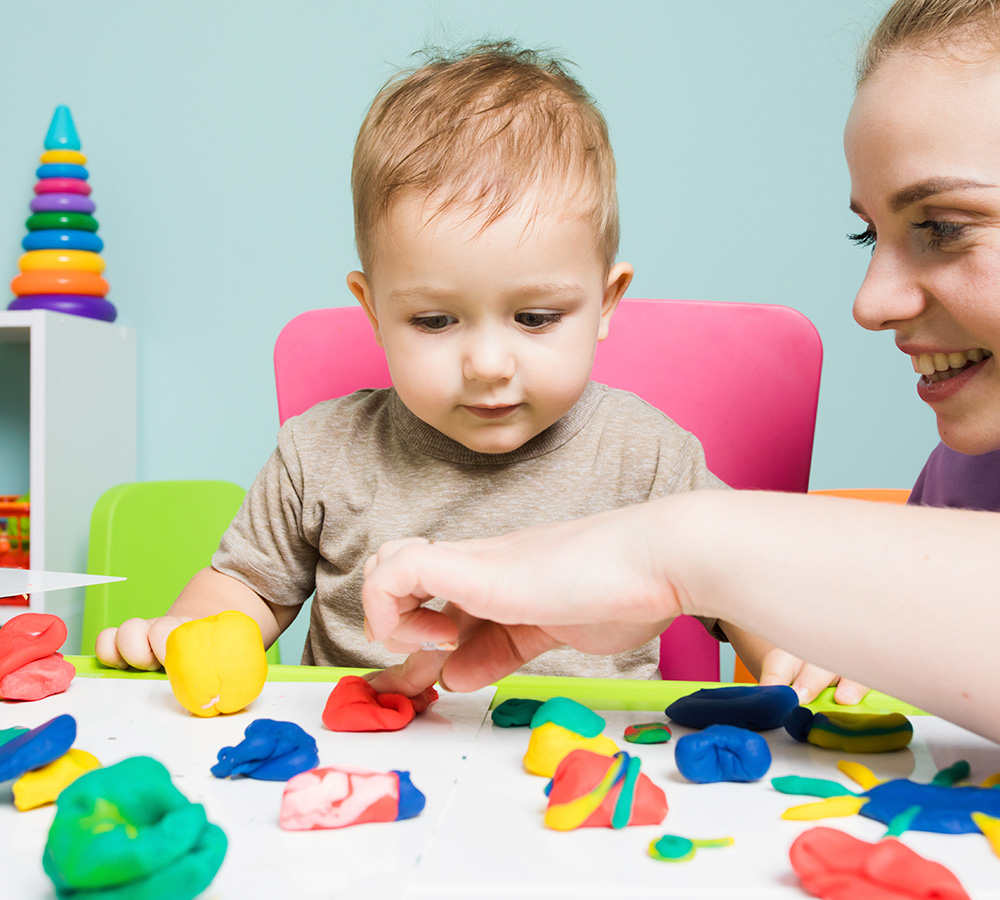 A child focused on playing with colorful modeling clay, while an teacher guides him, they engaged in creative play.