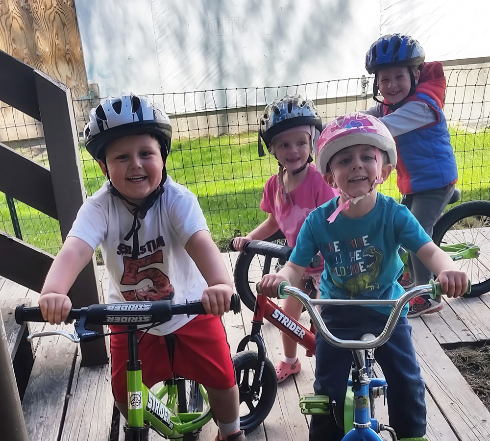 A group of kids happily ride bikes, all wearing helmets, enjoying a sunny outdoor adventure together.