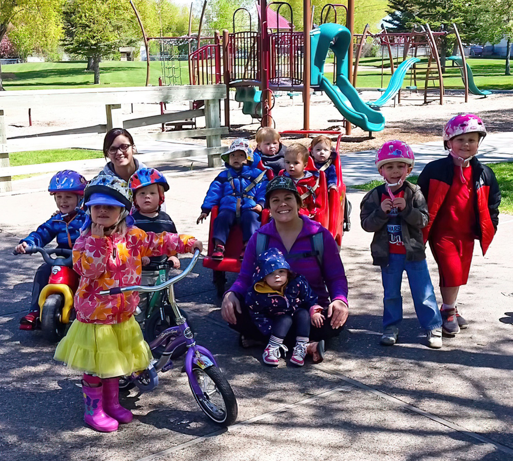 A group of children wearing helmet is playing outside, posing with teachers showcasing a fun day of activities and safety.