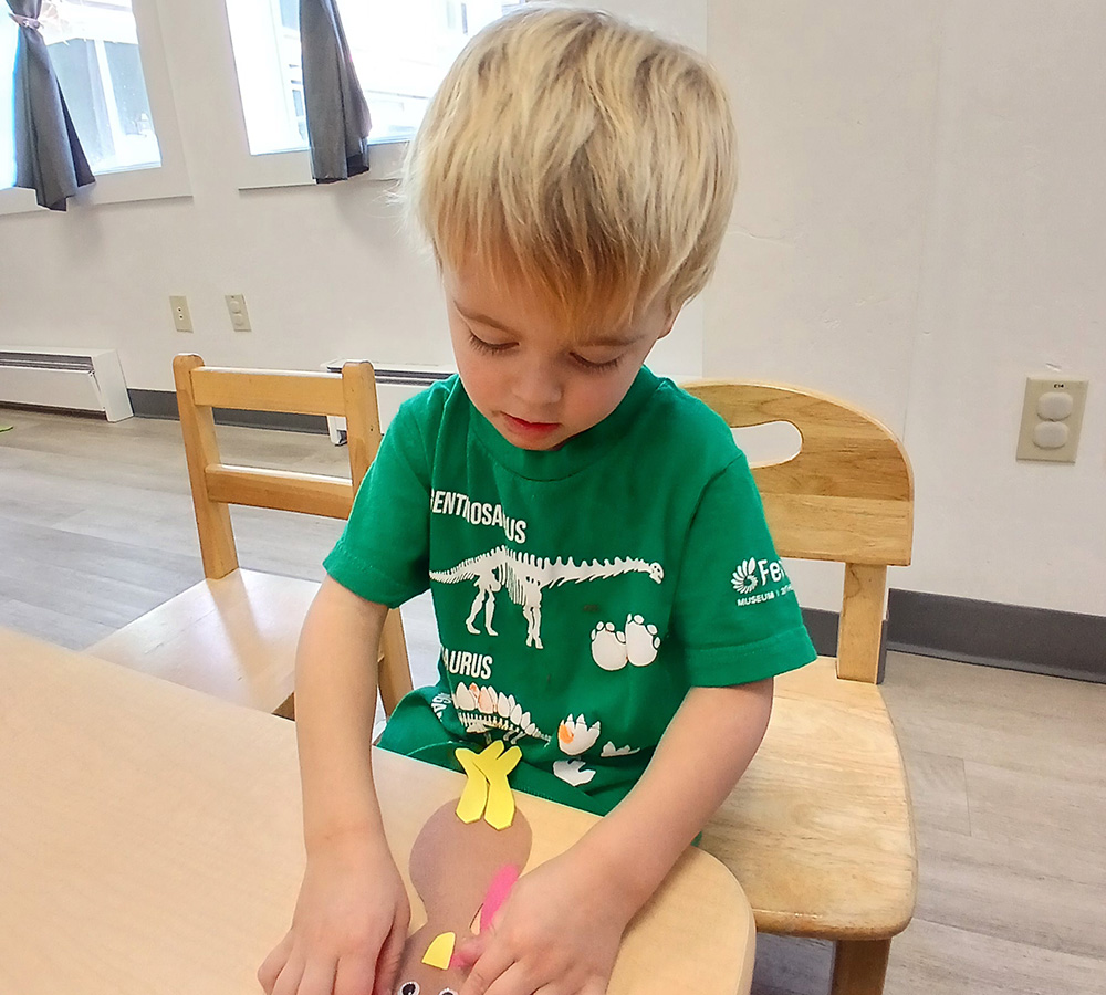 A boy is focused on crafting at a table, carefully placing colorful shapes as he engages in a creative activity.