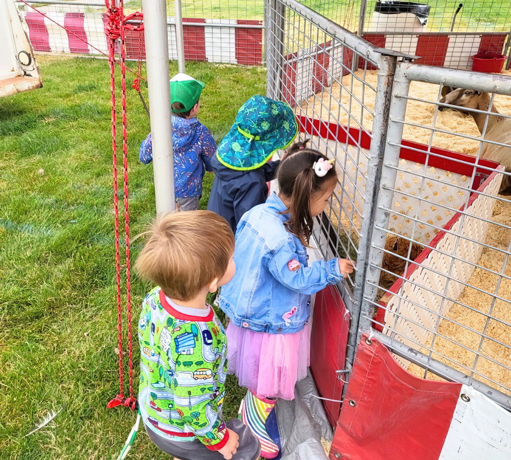 A group of children is gathered, eagerly reaching out to interact with animals, dressed in colorful outfits.
