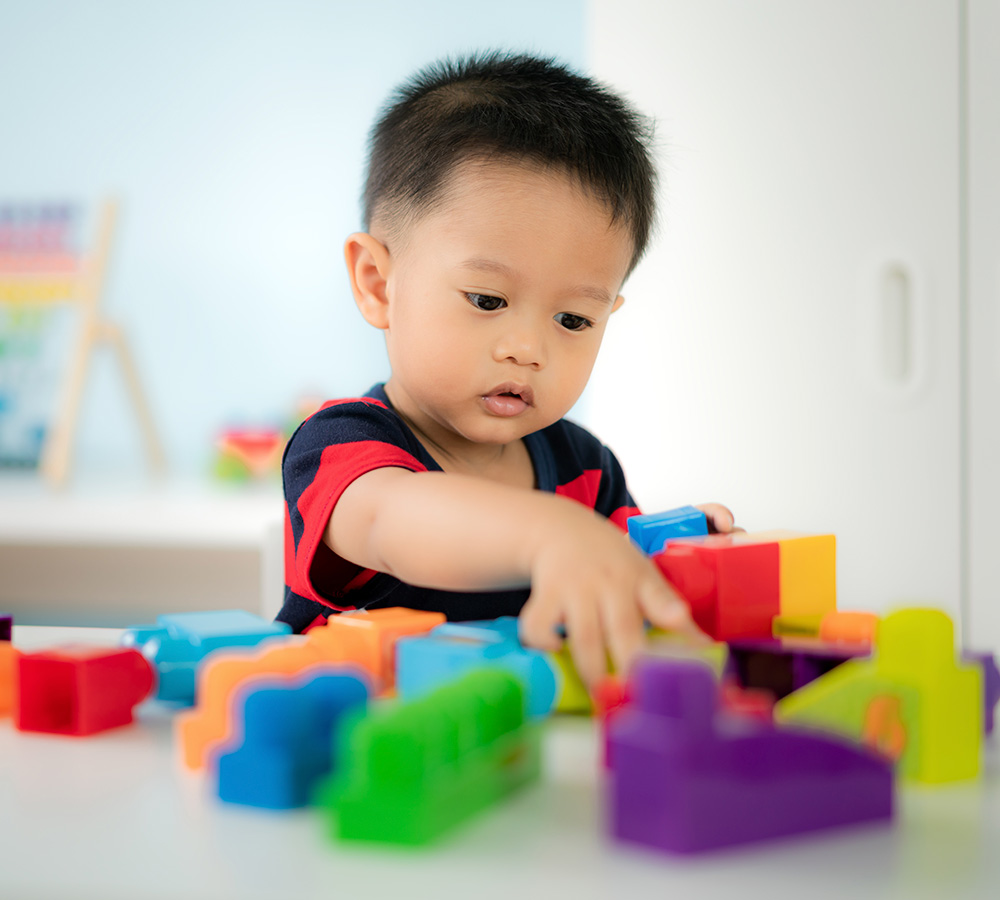 A boy is intently playing with colorful building blocks, demonstrating concentration and creativity in a bright setting.