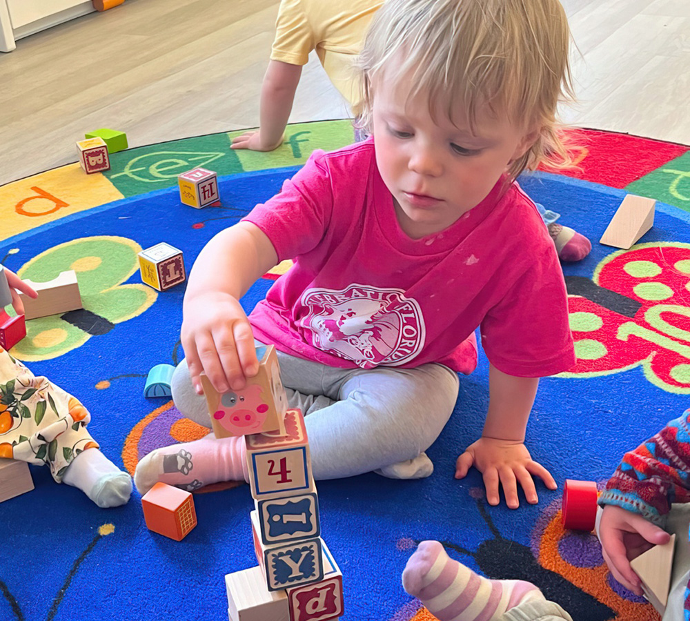 A toddler is focused on stacking colorful blocks on a vibrant play mat, showing concentration and creativity.