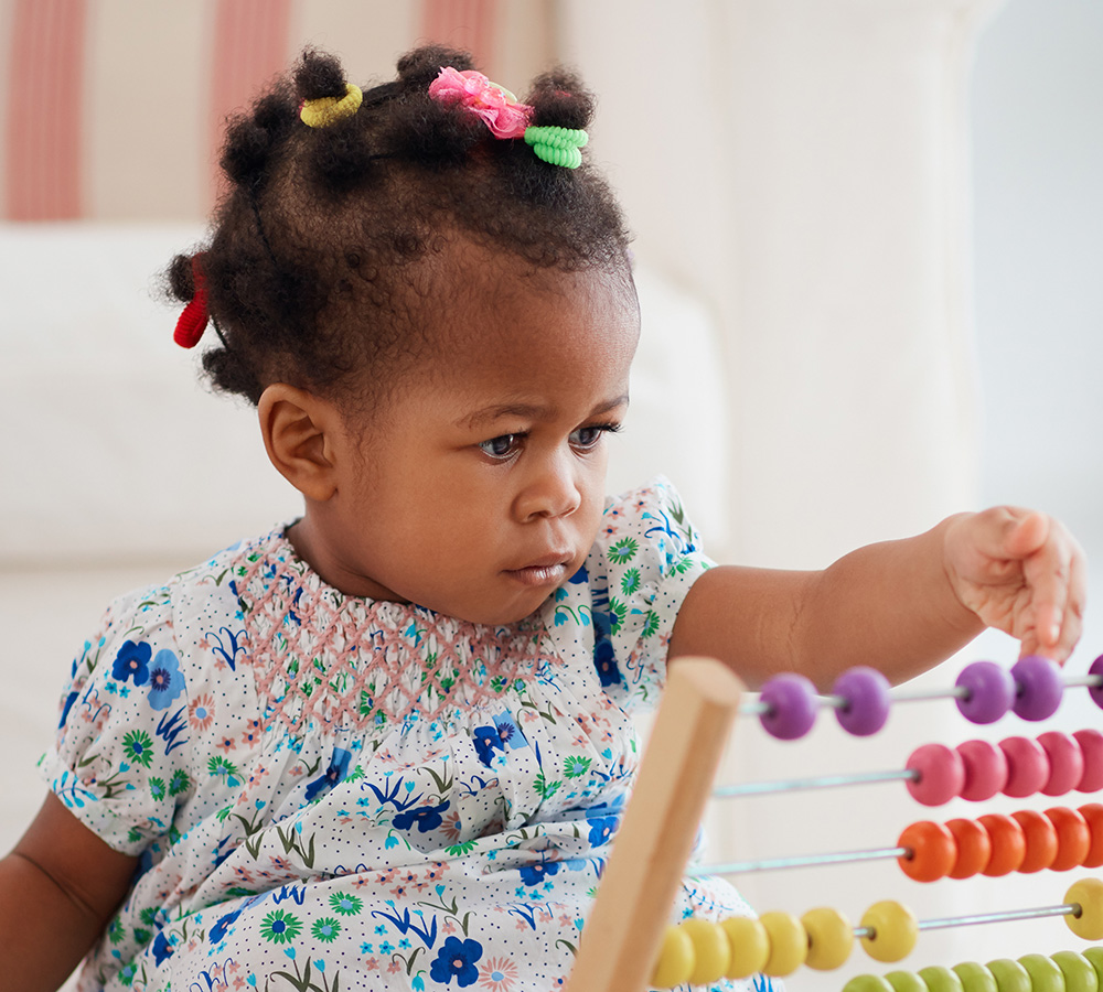 A young girl with styled hair is carefully playing with an abacus, concentrating on the colorful beads.