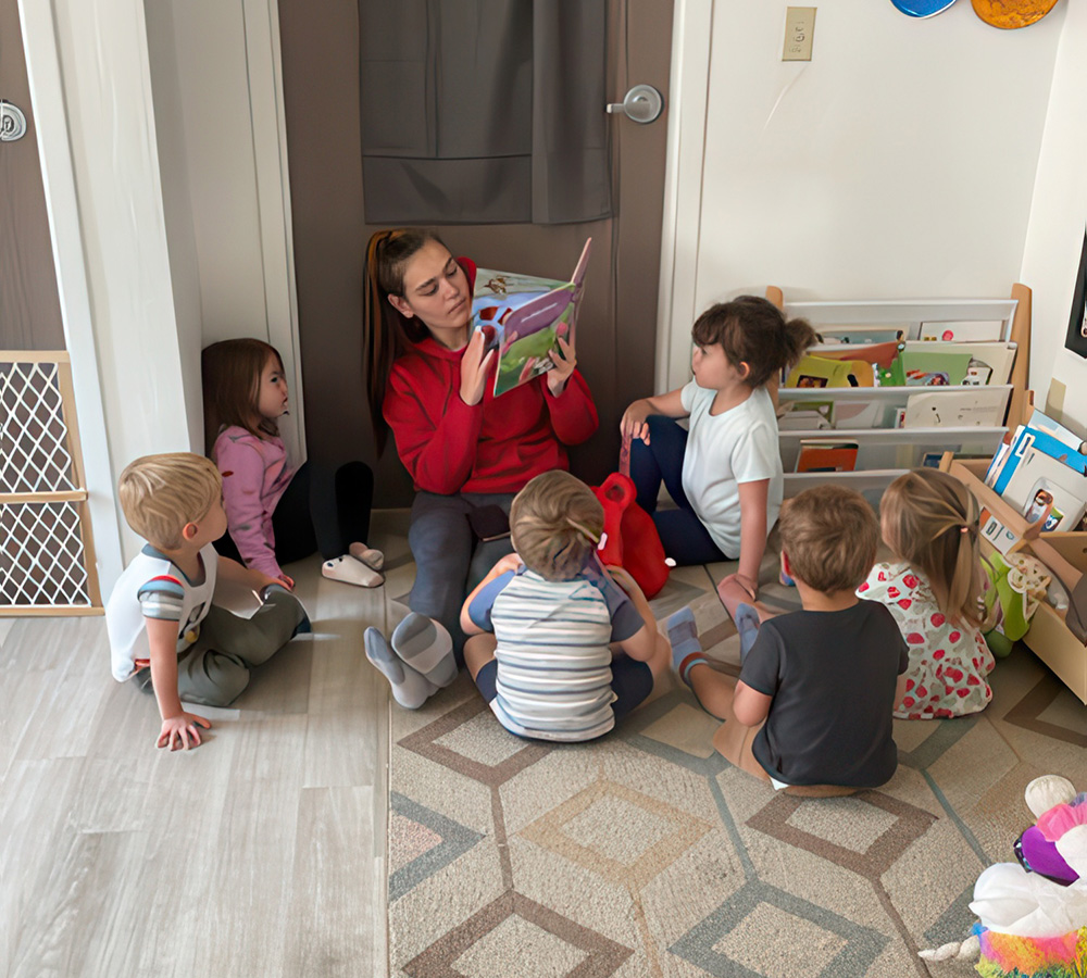 A teacher is reading a story to a group of children sitting on the floor, all engaged in the storytelling experience.