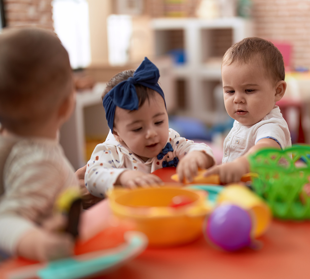A group of infants playing together at a table exploring toys, showing curiosity and collaboration.