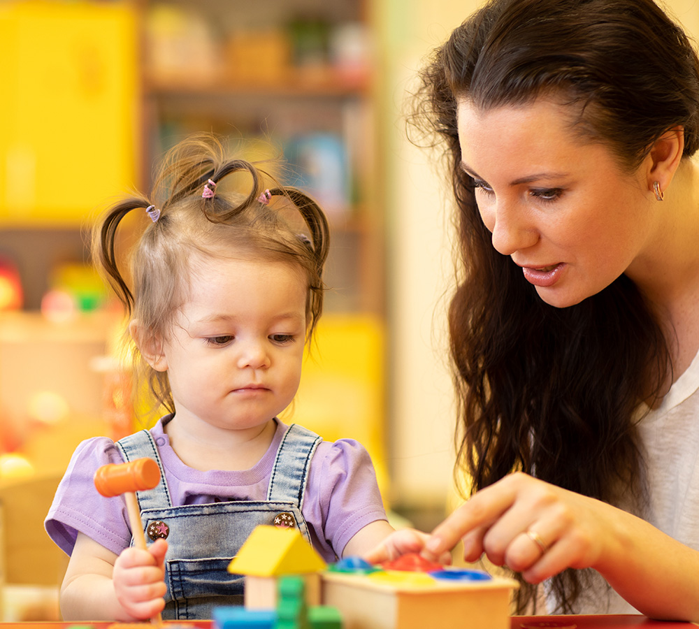A teacher is reading a storybook to two children, engaging them with animated storytelling and colorful illustrations.