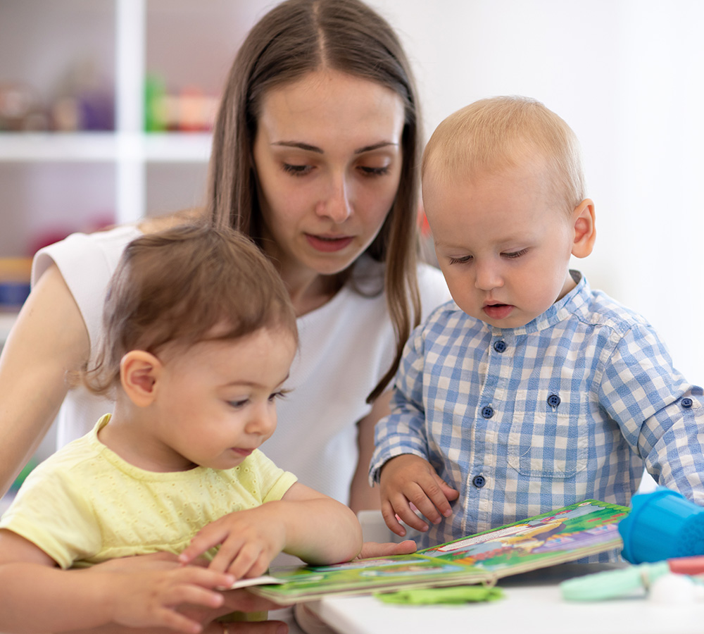 A teacher is reading with two children, both engaged and curious about the books.